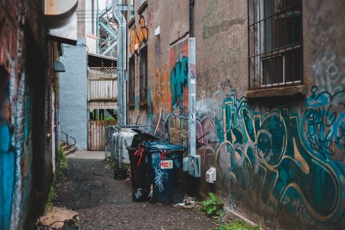 Free Garbage can on narrow street between aged houses with graffiti on shabby walls in town Stock Photo