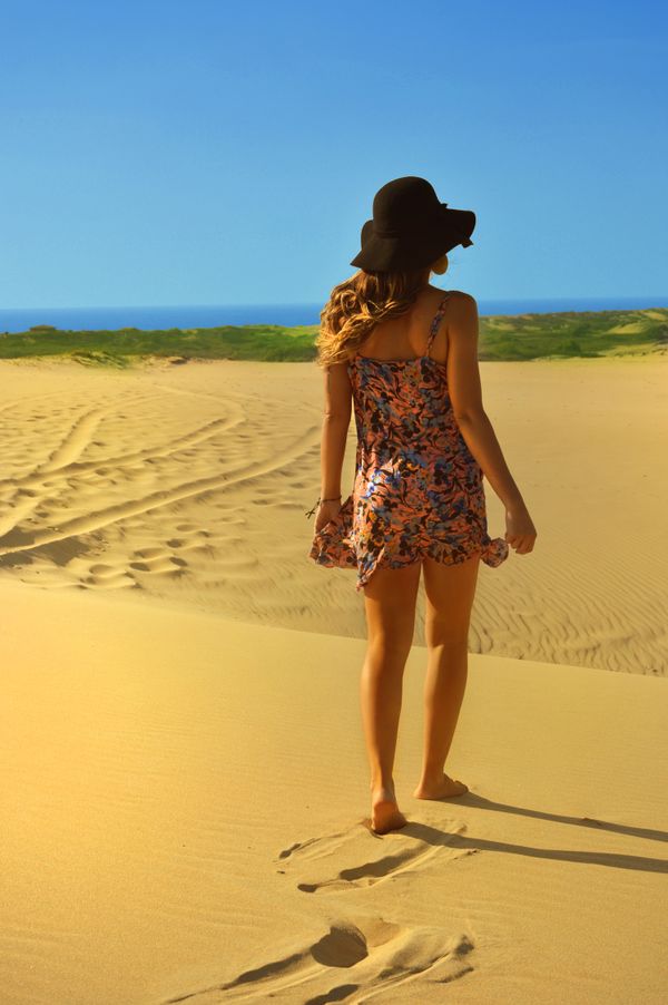 Woman in a sun hat walking across sand dunes — photo by Caio on Pexels