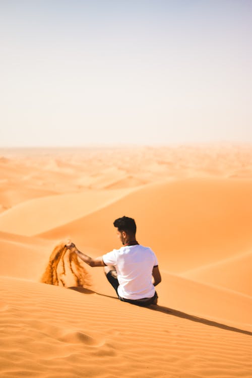 Man in White T-Shirt Sitting on Desert Dune