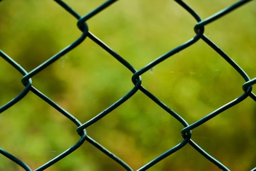 Free Close-up of a green chain link fence with a blurred natural background, suggesting security and boundaries. Stock Photo