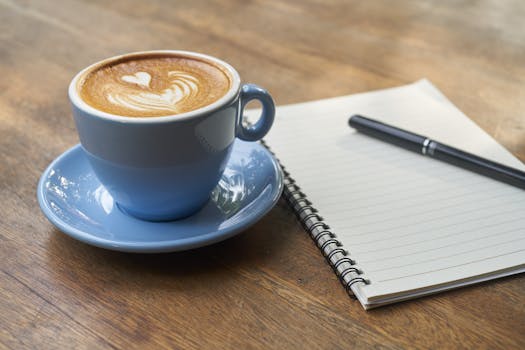 A beautifully crafted latte art next to a spiral notebook and pen on a wooden table.