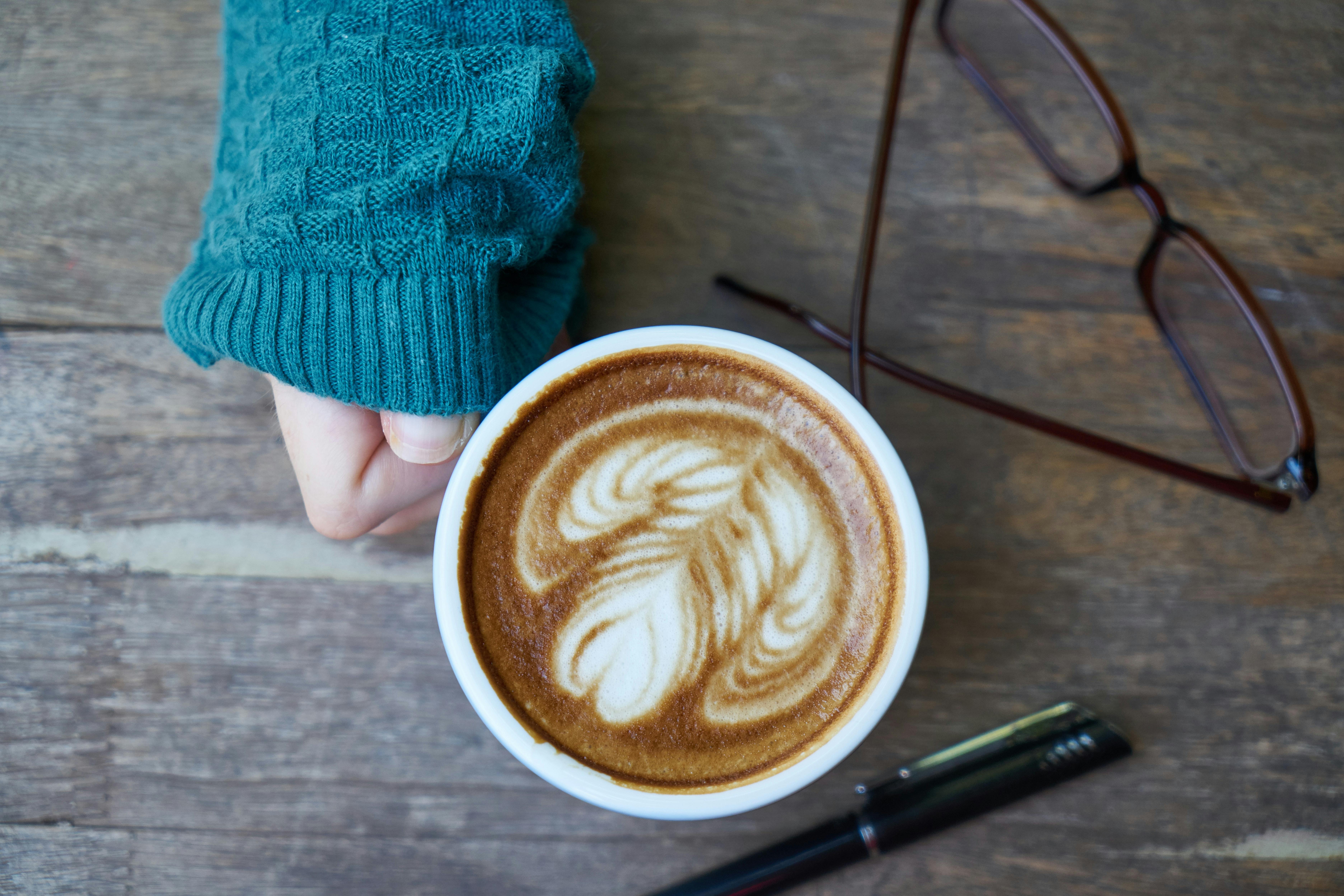 Free Top view of latte art coffee next to eyeglasses and pen on a wooden surface. Stock Photo