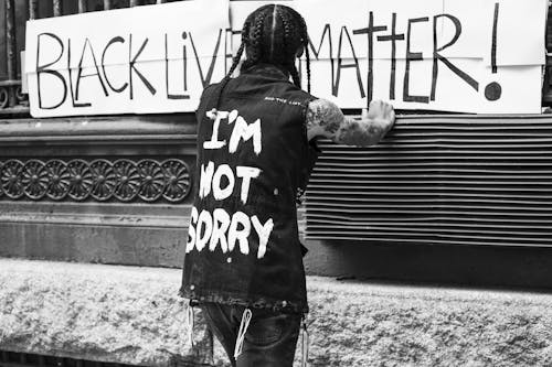 Back view of unrecognizable tattooed guy standing on street in front of banner with Black Lives Matter inscription