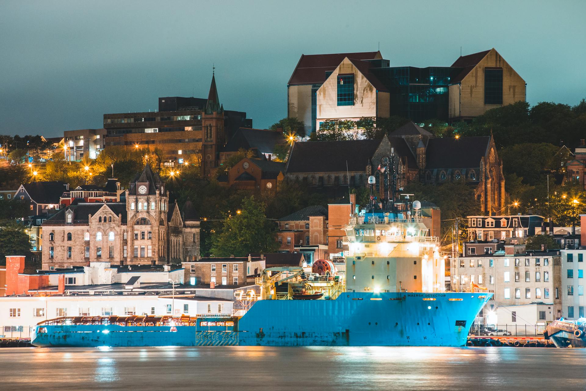 Modern vessels floating in harbor of St John s city near aged churches and residential buildings in evening