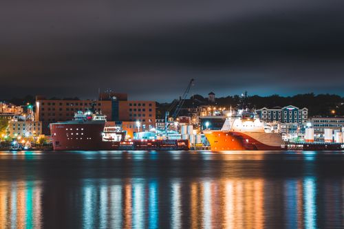 Free Modern cargo vessels moored in harbor of city with colorful lights reflecting on sea at night Stock Photo
