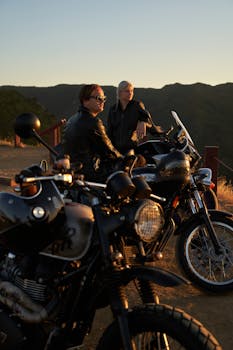 Couple sitting on motorcycles enjoying a scenic sunset view in nature.