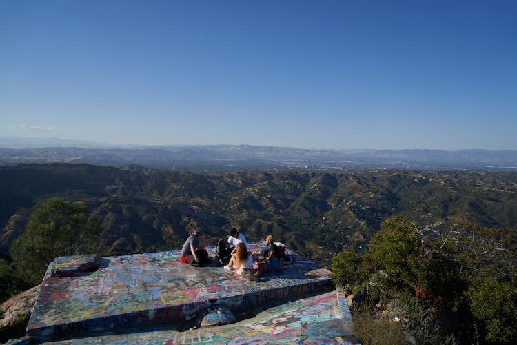 People Sitting On Lookout Deck With Mountains View