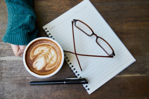 Latte Art in Cup Beside Paper and Pen