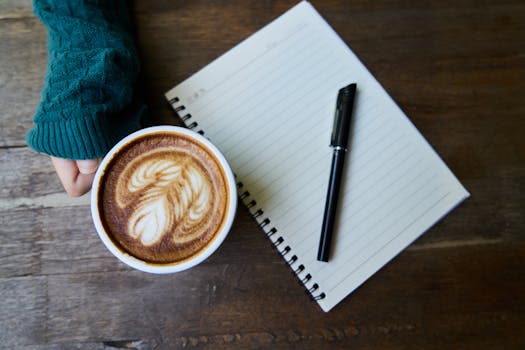 A cozy café scene featuring a latte with art, next to a notebook on a wooden table.