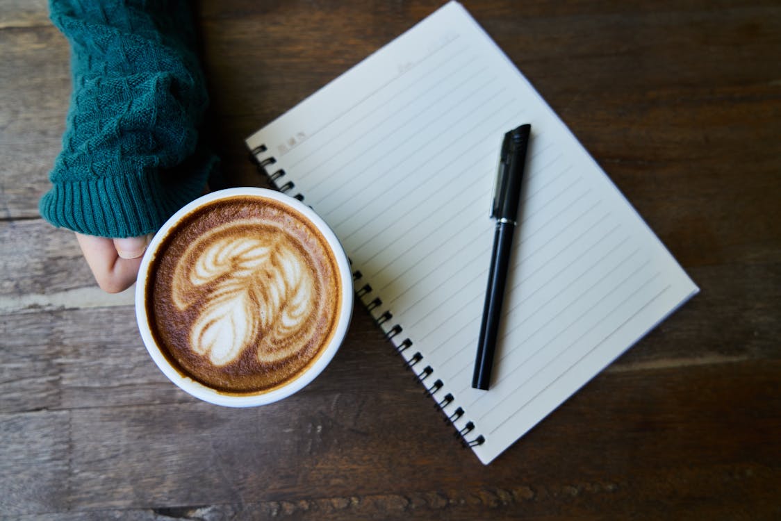Free Black Pen on Ruled Paper Beside Cup of Latte Stock Photo