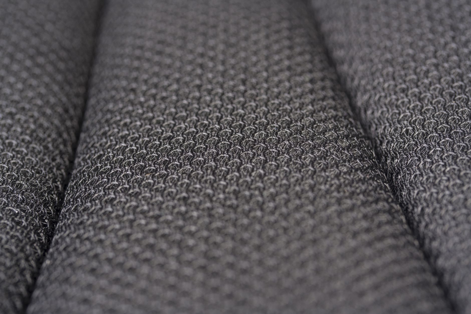 Gros plan sur un tissu matelassé gris foncé formant des plis, surface textile d'un matelas