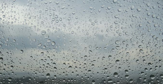 Close-up of raindrops on a window, forming an abstract pattern against a cloudy sky.