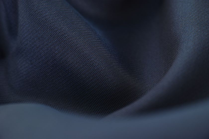 Close-up of a navy filament cloth in soft folds, a fine even weave carrying a low sheen.