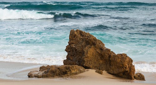 Sandy seashore with rough rock washing by foamy waves