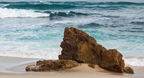 Free Foamy waves of powerful stormy sea crashing near rocky formation on sandy beach in daytime Stock Photo