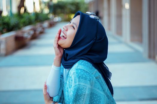 A woman wearing a hijab laughs joyfully outdoors, capturing a moment of happiness and cultural expression.
