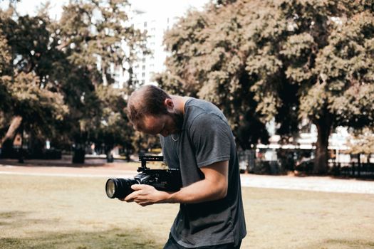 Focused photographer using a camera in a picturesque park setting, capturing unique outdoor scenes.