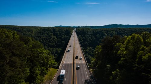 Free Aerial view of various vehicles riding on highway surrounded by lush green trees against blue sky on sunny day Stock Photo