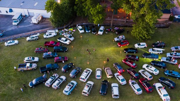 From above of various cars parked in circle on green lawn in park near anonymous people