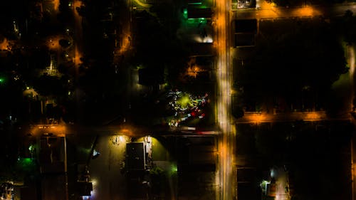 Aerial view of brightly illuminated city streets with silhouettes of houses at dark night