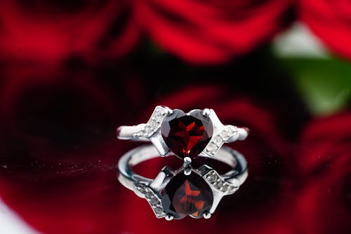 Ring with small crystals and red ruby stone placed on reflective surface against red roses