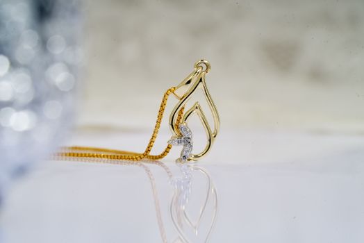 Shiny golden pendant on chain on reflecting table