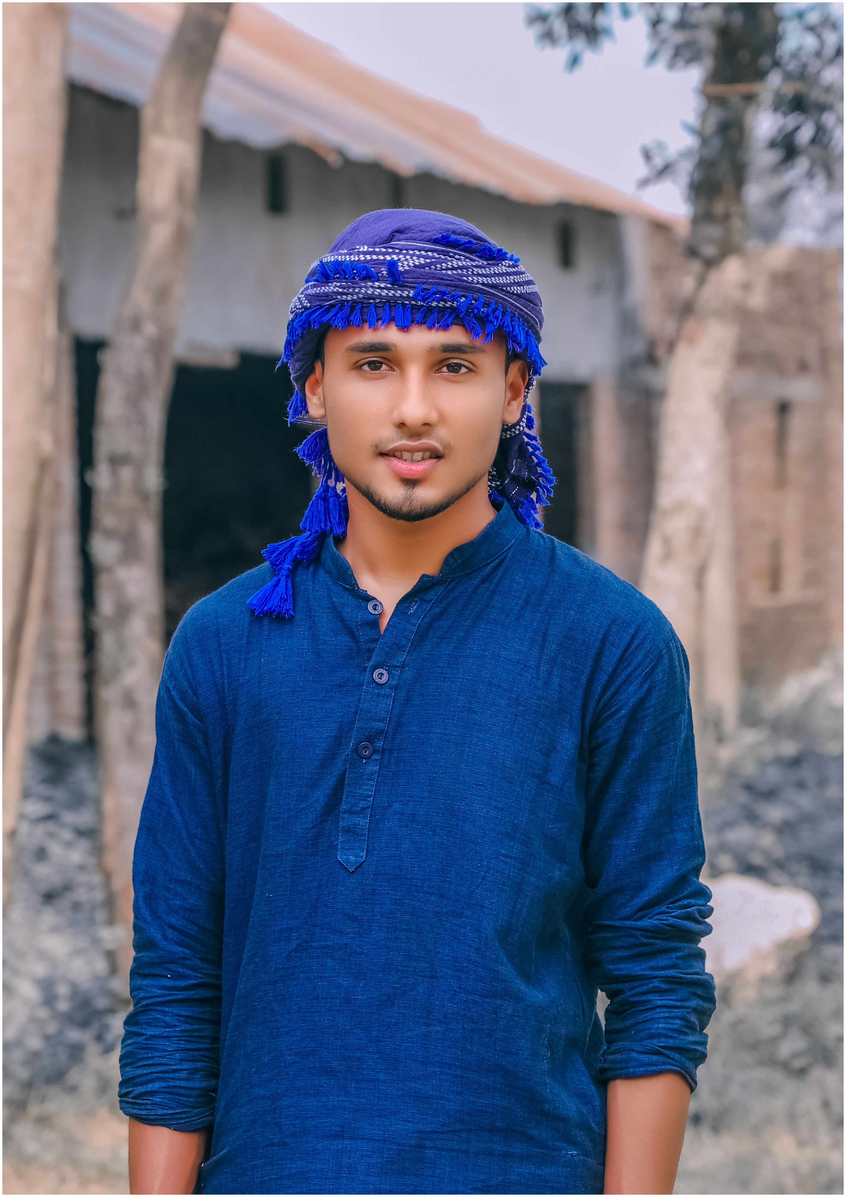 Young ethnic male in traditional turban and standing against weathered stone buildings of small old town
