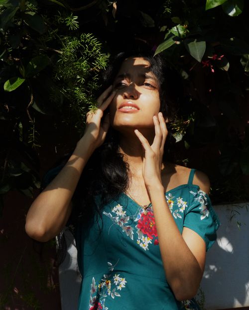 Free A woman in a floral dress stands amidst greenery, embracing natural light in a serene outdoor setting. Stock Photo