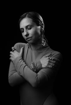 Black and white portrait of a woman embracing herself with an elegant and serene expression.