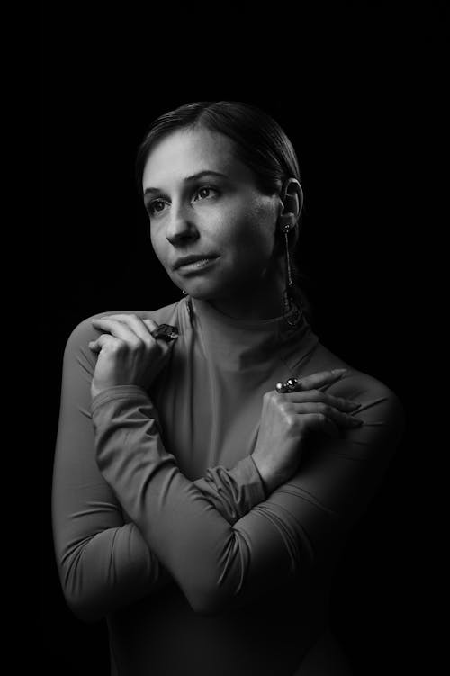 Free Black and white of young female crossing arms on chest and looking away while standing on black background Stock Photo