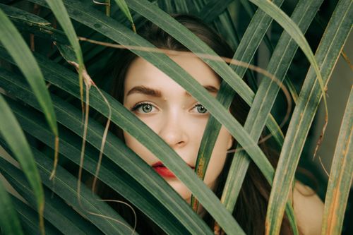 Free Close-up of a woman's face partially hidden by green leaves for an artistic look. Stock Photo