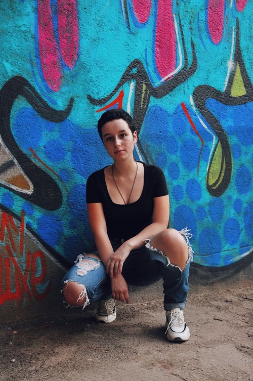 Free Full body of cool young female sitting on hunkers next to graffiti wall and looking at camera Stock Photo