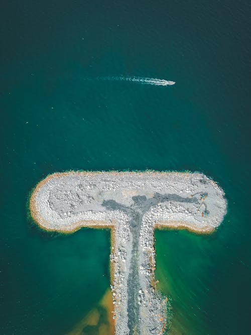 Aerial landscape of small empty artificial peninsula covered with pebbles in bright turquoise bay