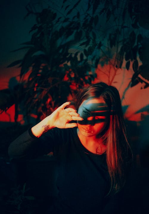 Pensive young female in black shirt holding palm in front of face while hiding from bright light