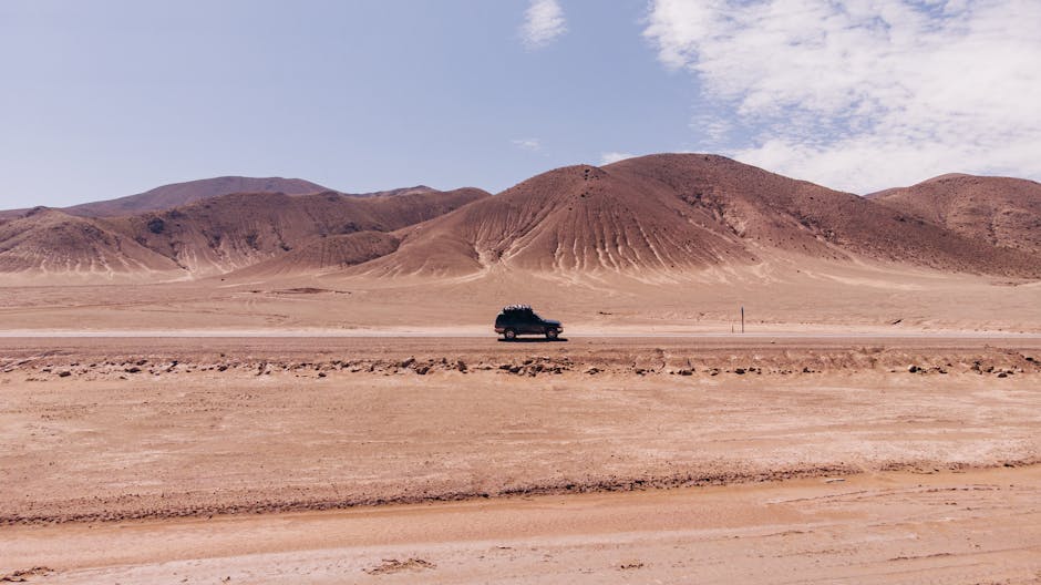 riviera maya hidden gems off the beaten path - SUV driving through arid desert landscape in Argentina with hills in the background.