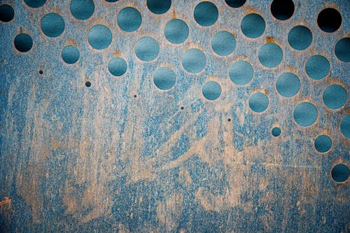 Textured backdrop of blue metallic wall with scratches and rusty round shaped holes