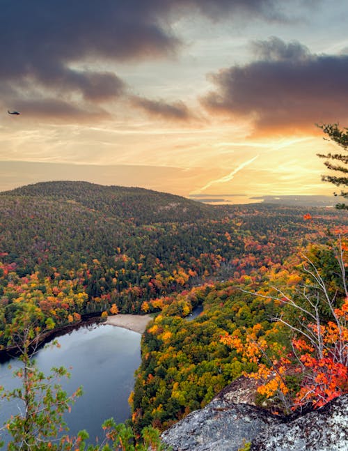 Spectacular scenery of peaceful lake surrounded by lush colorful trees against picturesque cloudy sunset sky in autumn