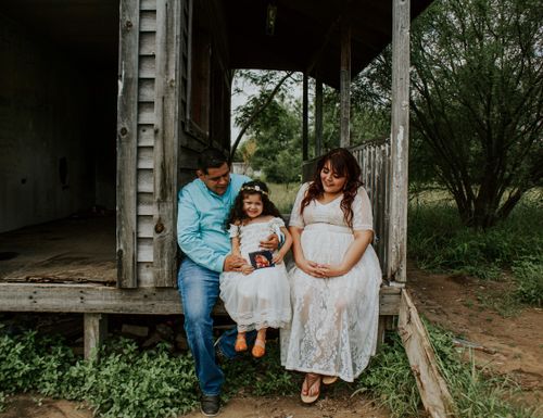 Free Smiling father and pregnant mother sitting with happy daughter in dress on wooden terrace Stock Photo