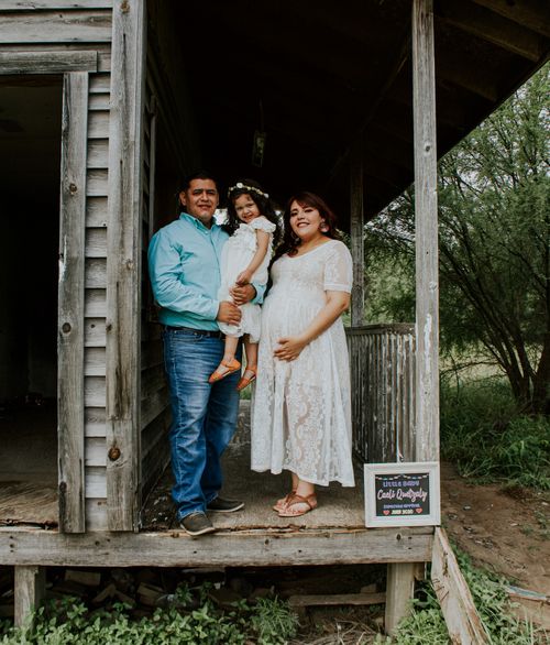 Free Happy family with expectant woman and smiling girl standing on wooden porch while looking at camera Stock Photo