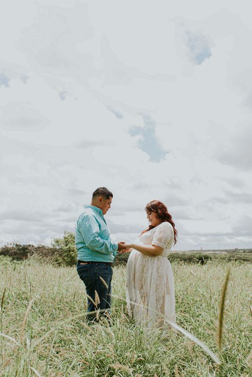 Free Side view of chubby male holding hands of stylish expectant female beloved on grass meadow under cloudy sky Stock Photo