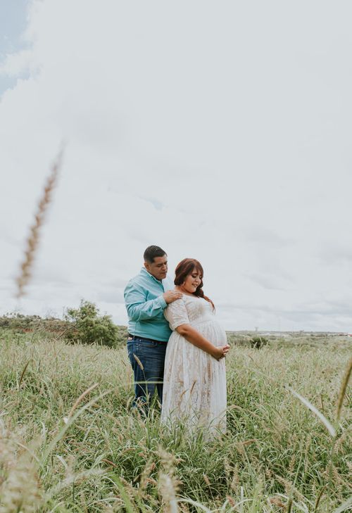 Free Side view of expectant female in stylish dress touching tummy while standing near plump boyfriend in field under sky Stock Photo