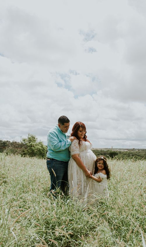 Free Plump man embracing expectant beloved with smiling girl in field in countryside under cloudy sky Stock Photo