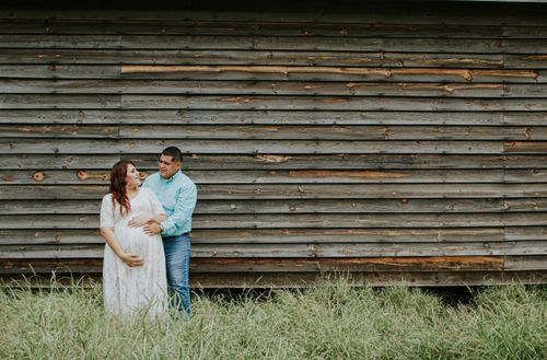 Free Smiling male embracing belly of expectant female partner while looking at each other on grass near shabby wall Stock Photo