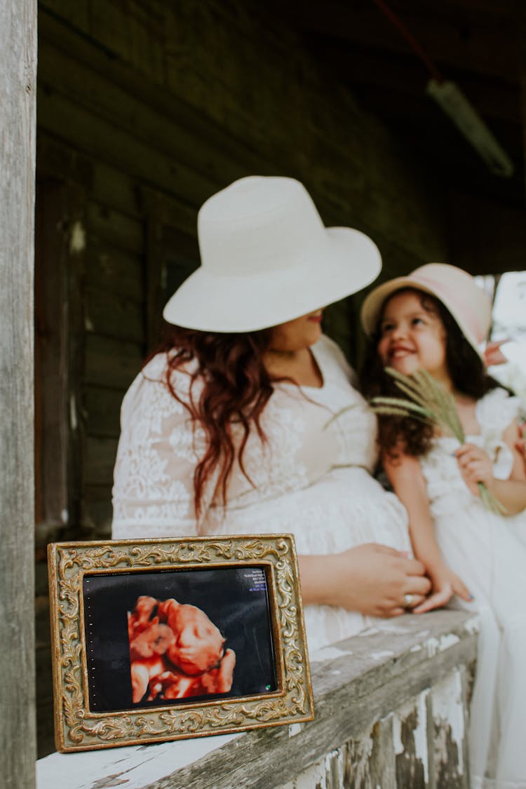 Anonymous Pregnant Mother With Smiling Daughter Near Photo Of Fetus