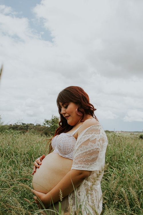 Free Side view of reflective expectant female in underwear touching gently big tummy on grass in countryside under cloudy sky Stock Photo