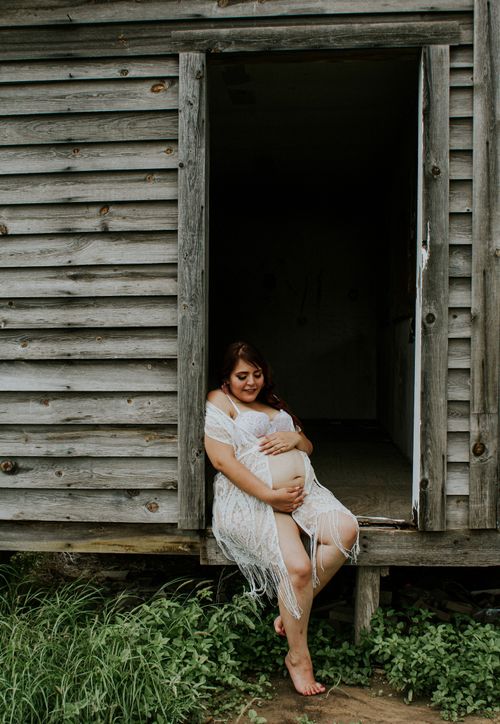 Free Smiling expectant female in lingerie touching gently tummy while sitting on floor of old construction Stock Photo
