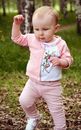 Funny little child in pink clothes with raised arm strolling on grass in summer while looking down