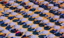 从阳光明媚的海岸鸟瞰蓝白条纹沙滩伞