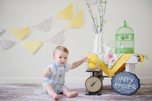 Baby Sitting on Floor Surface Near Table and White Wall