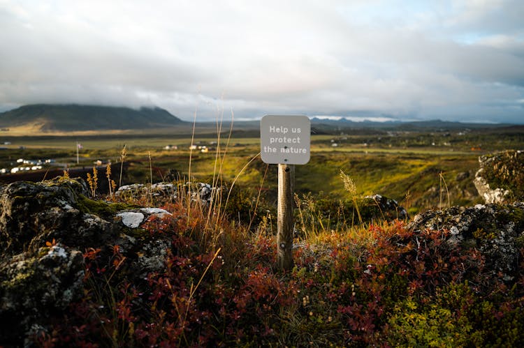 Wooden Post Sign On A Field Under White Clouds